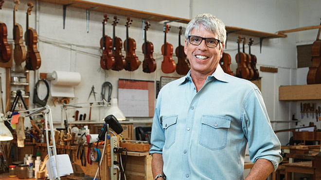 Man in a violin shop, smiling wearing a blue shirt