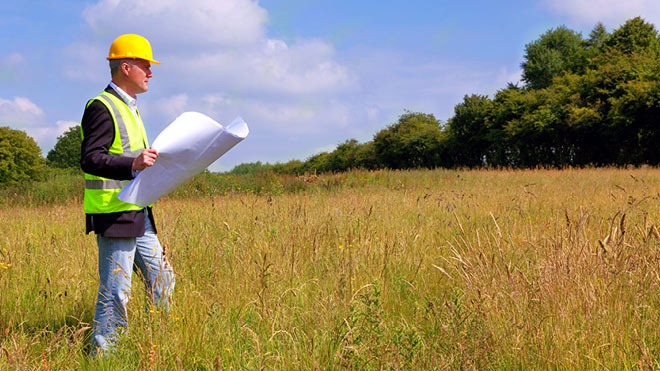 Man on open land looking at house plans