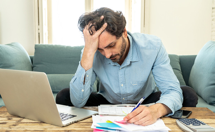 Man sitting on a couch, hand in hair, paying paper bills next to laptop