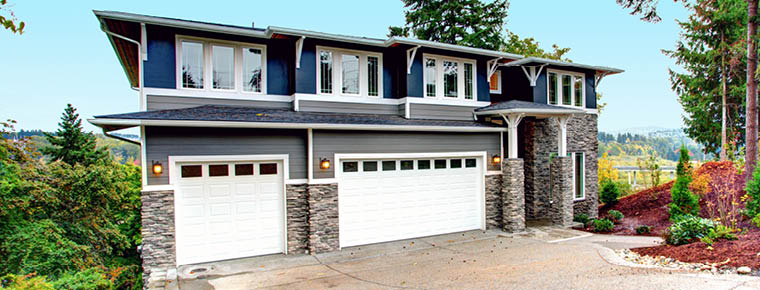 A large blue house with white trim, stone veneer along the lower third and two white garage doors.