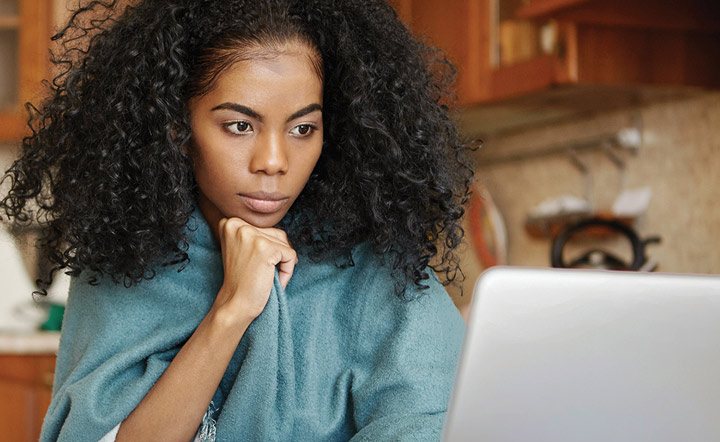 Woman with chin resting on her hand concentrates while looking at a laptop screen