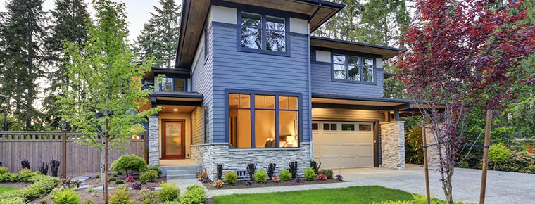 Photo of a modern house with stone veneer along the bottom, vinyl-framed windows, and a four-panel garage door with windows across the top.