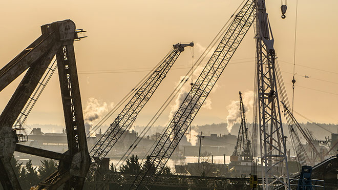 Cranes and bridges along the Lower Duwamish Waterway with steam plumes from industry operations in the background. The sky is brown and hazy from wildfire smoke.