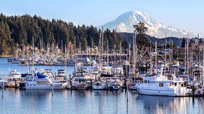 Image is a landscape view showing boats in Gig Harbor. The sky is cloudless and you can see Mount Rainer in the background.