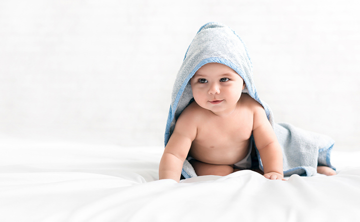 Newborn baby draped in a light blue towel, crawling on a bed with white sheets