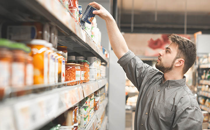 A man takes a can off the top shelf in a grocery aisle.