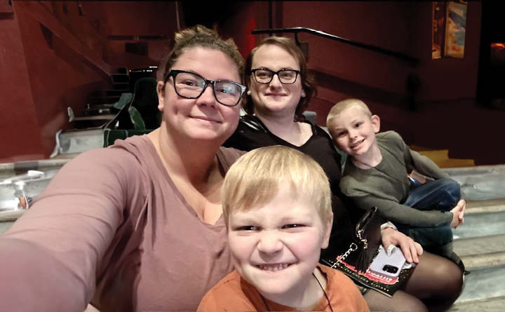 BECU employee Amanda G and her family (two young boys and her partner) pose for a selfie in a theater setting. 