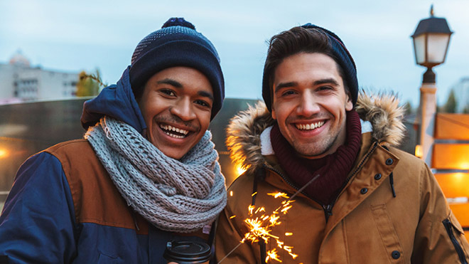 Two smiling men wearing beanies and a sparkler.