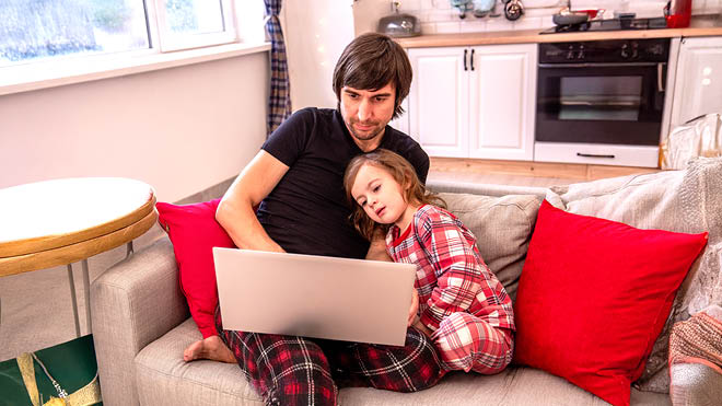 A man and his child sitting on a couch looking at a laptop screen.